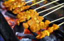 Satay chicken skewers grilling over hot charcoal, showcasing the cooking process by FoodByWayne